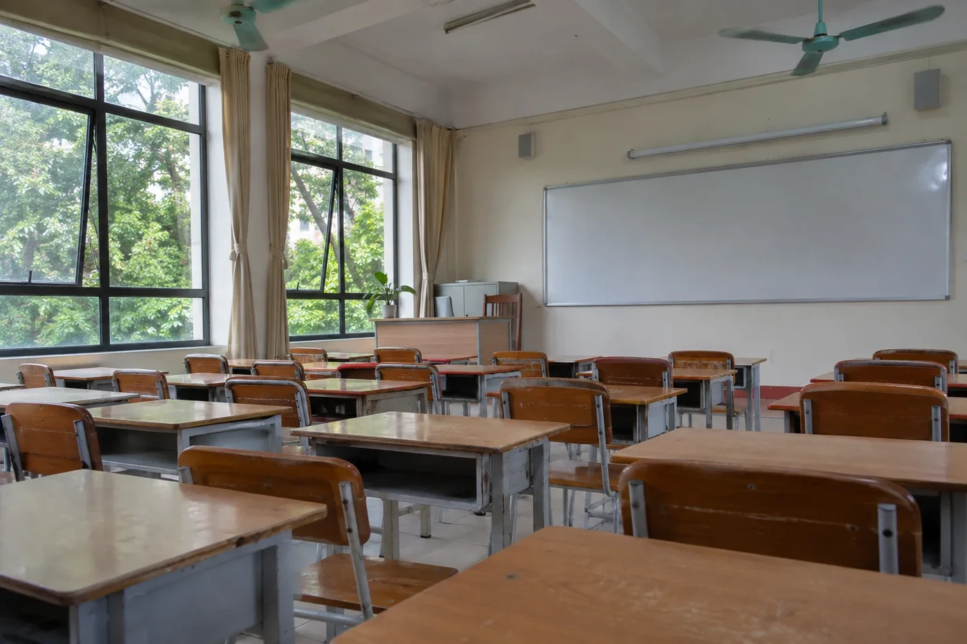 Empty classroom with wooden desks, ceiling fans and a whiteboard