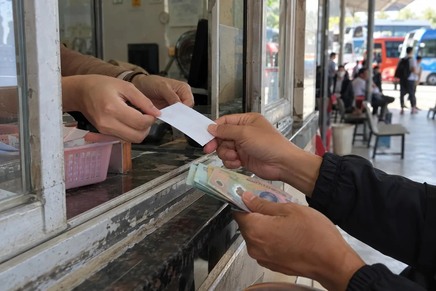 Hands exchanging cash and a paper ticket at a bus station window