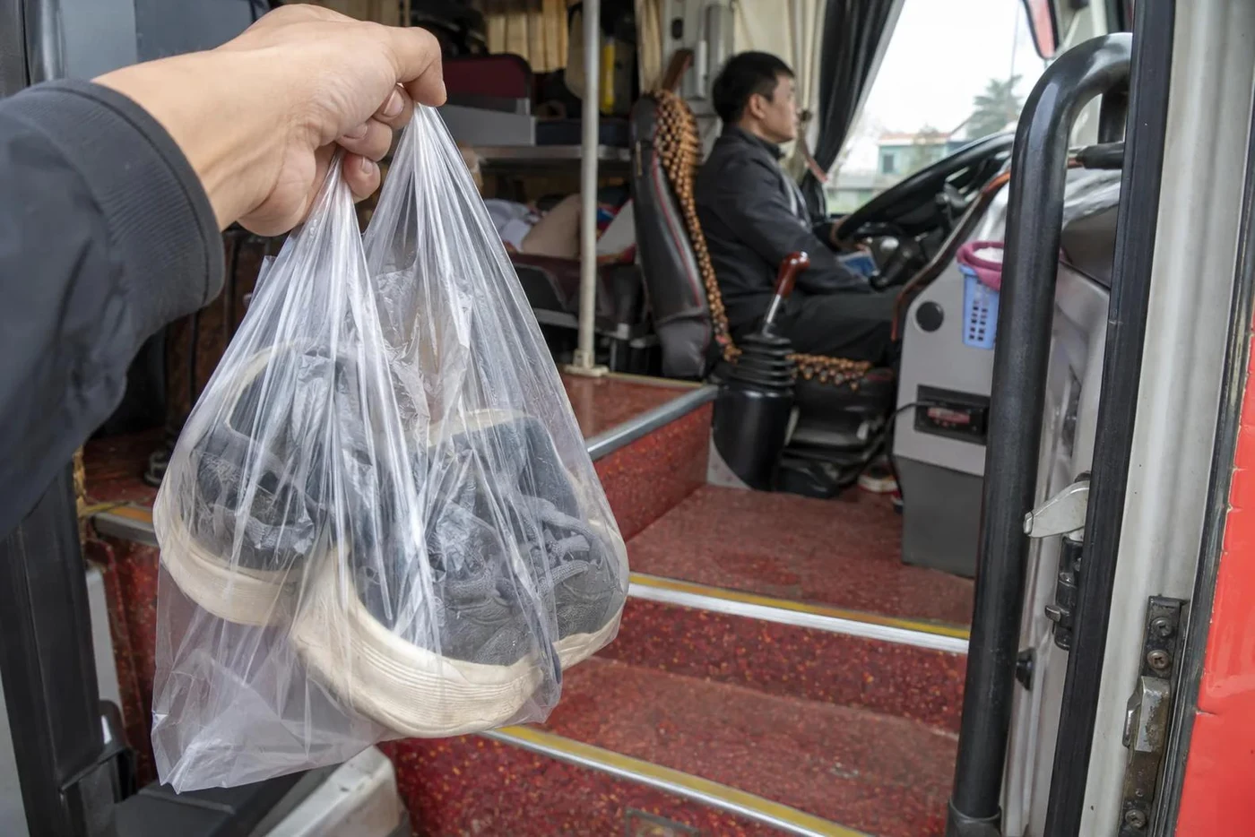 Hand holding sneakers in a plastic bag at the door of a bus