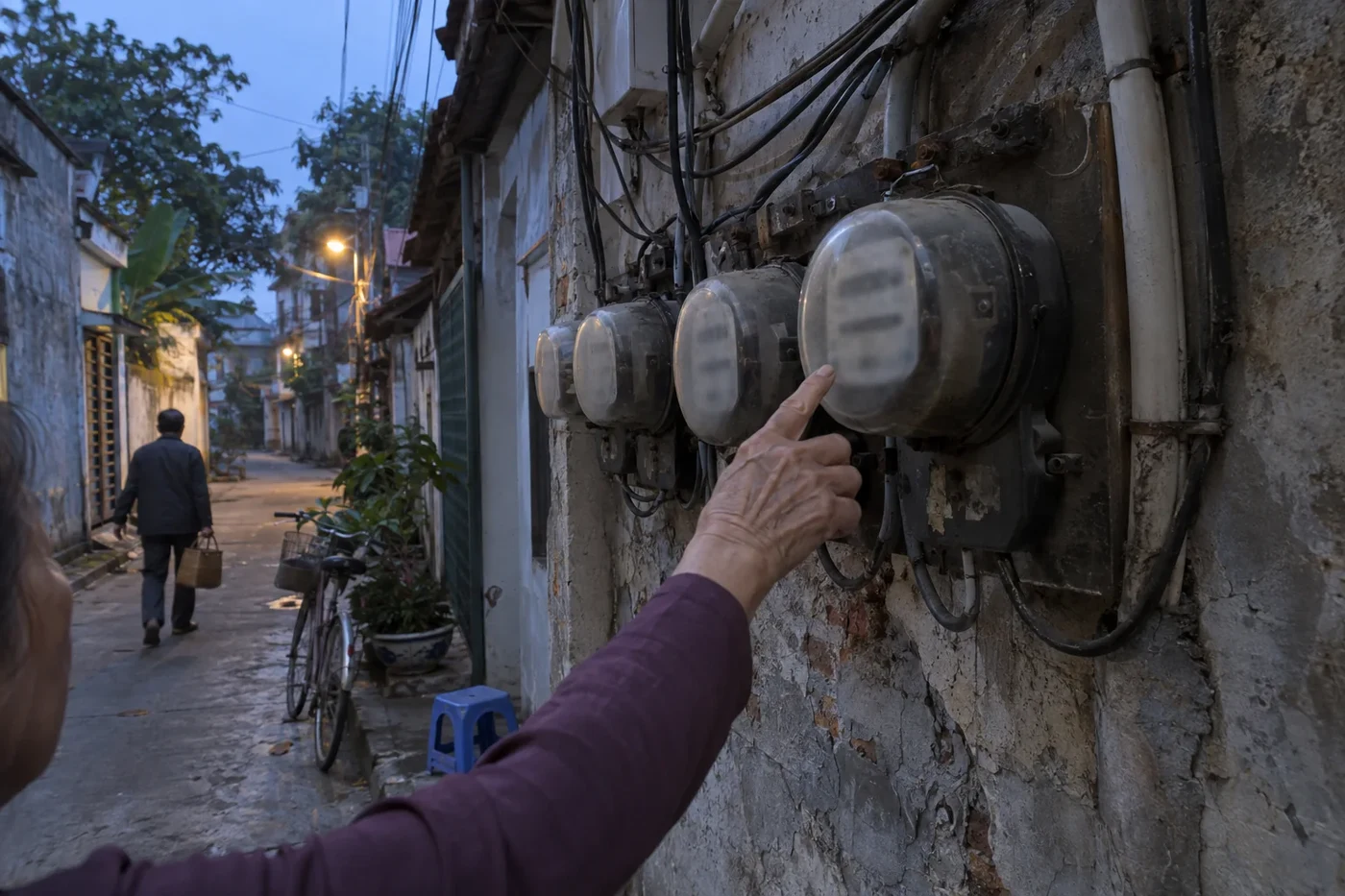 Hand pointing at a row of old electricity meters on an alley wall
