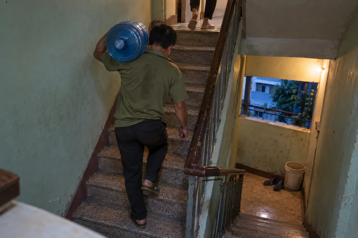 Man carrying a 20-litre water bottle up a stairwell on his shoulder
