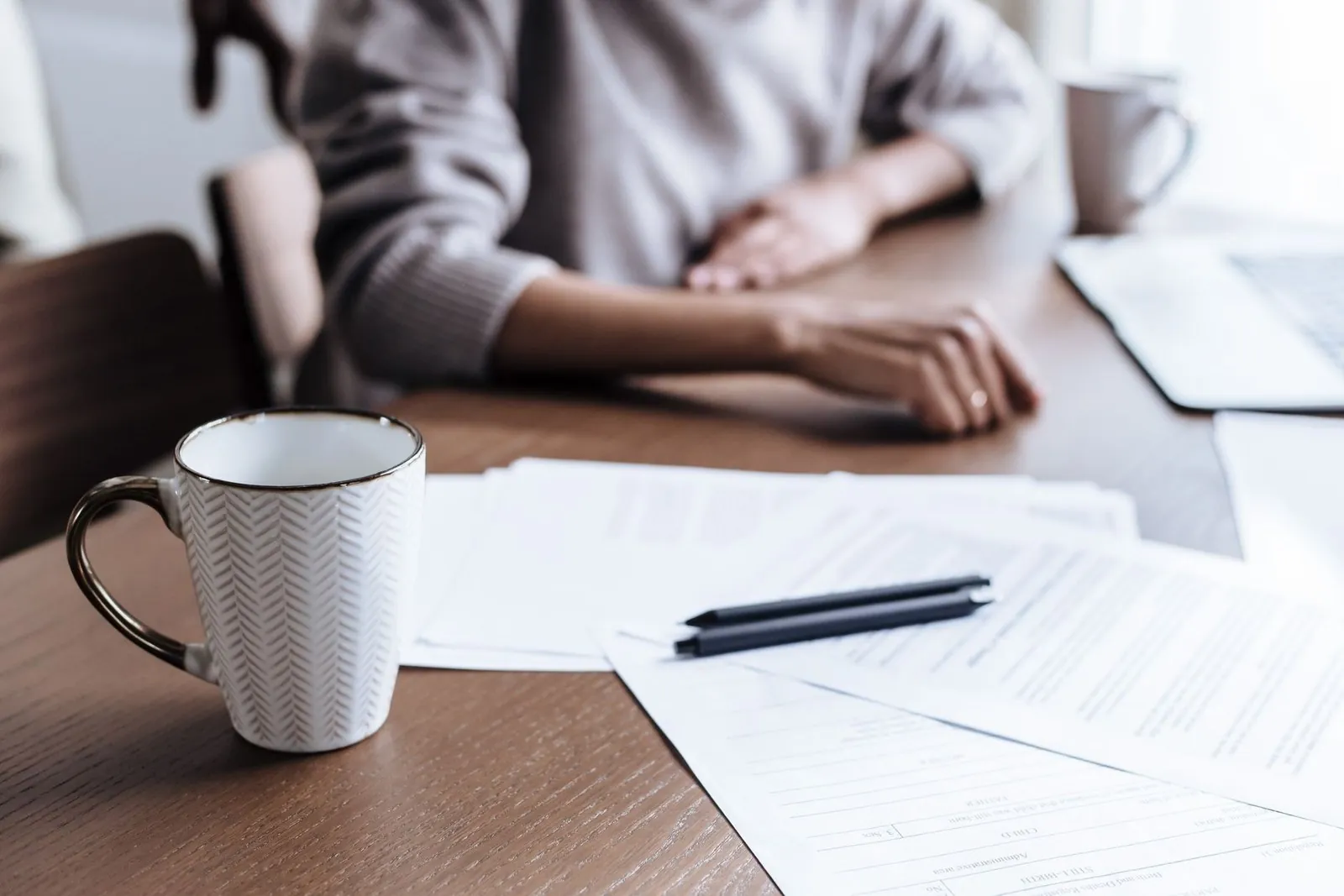 Coffee mug beside paperwork and a pen on a wooden desk with a laptop