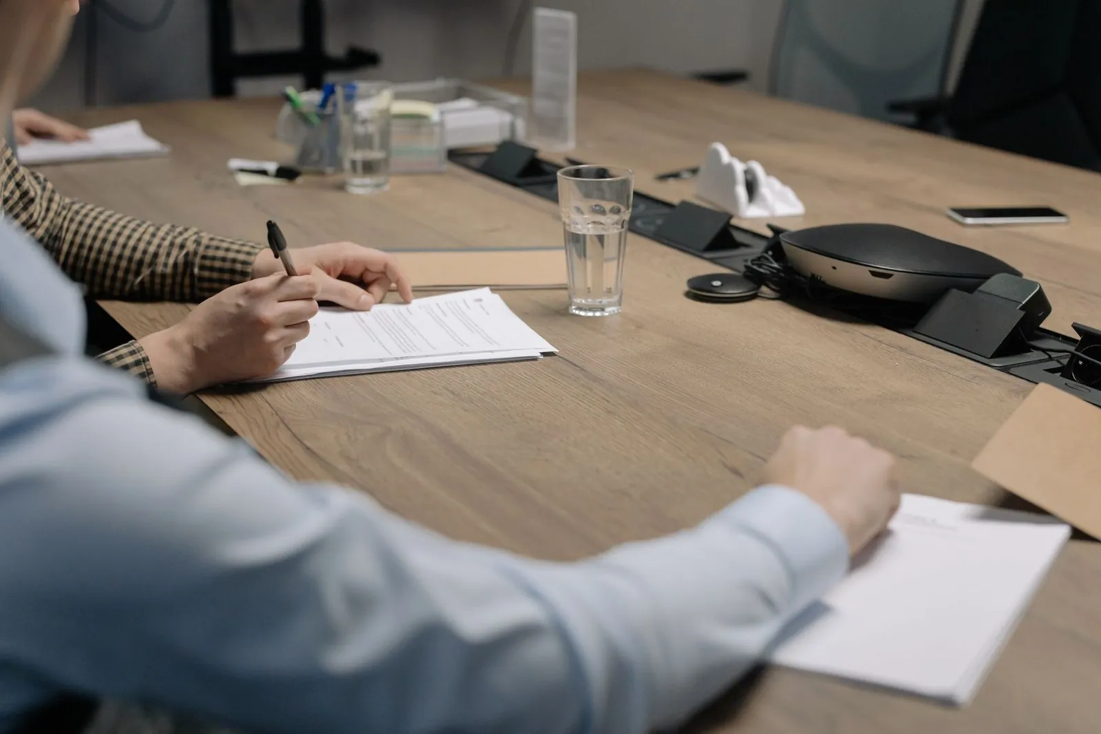 Two people reviewing and signing paperwork across a wooden office table
