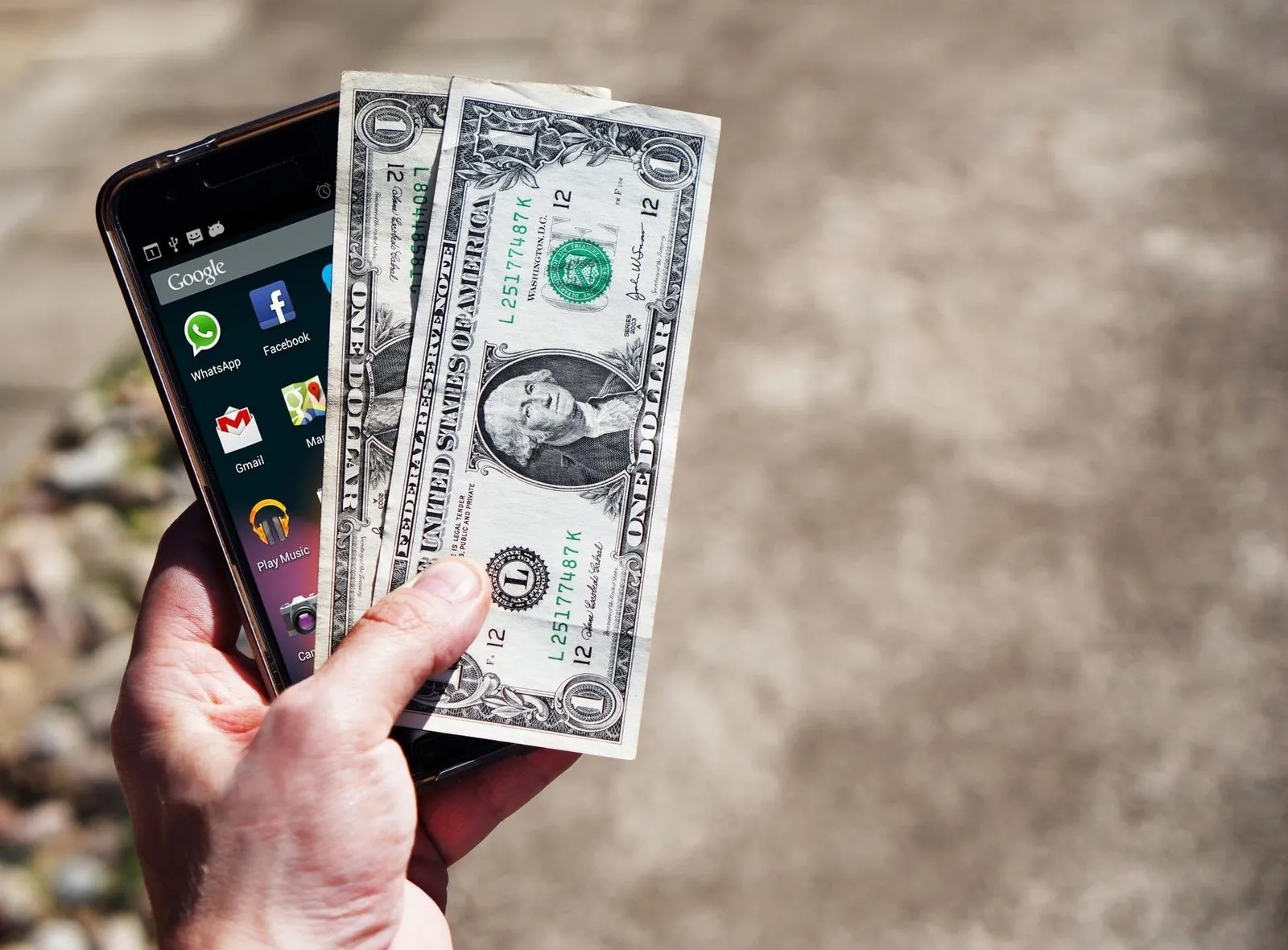 Hand holding a smartphone and two US dollar bills