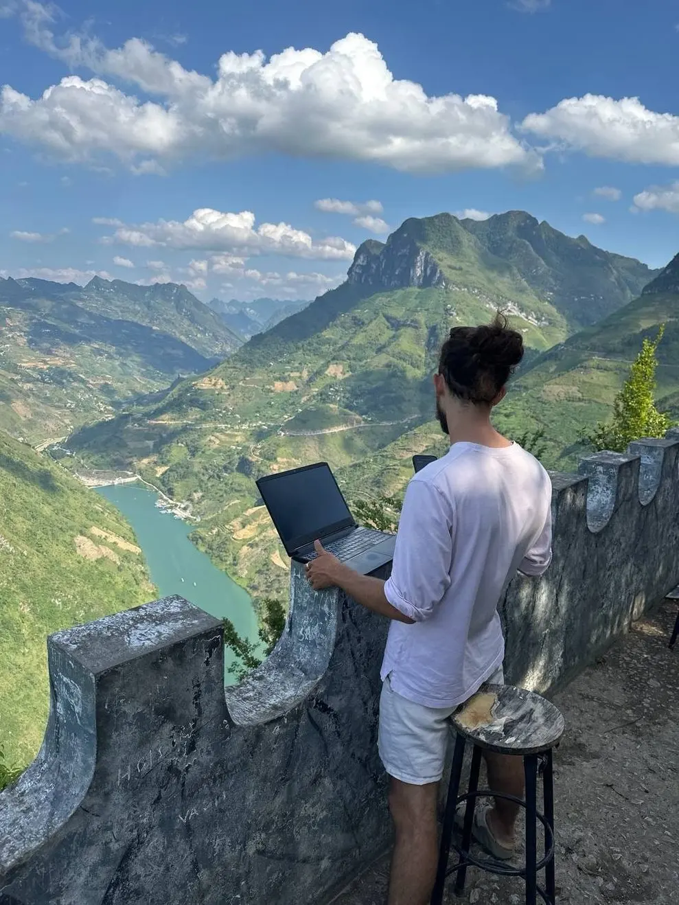 Man working on a laptop at a mountain viewpoint in Ha Giang, Vietnam