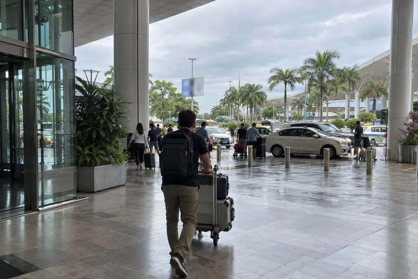Traveller pushing a luggage trolley across a wet airport arrivals forecourt