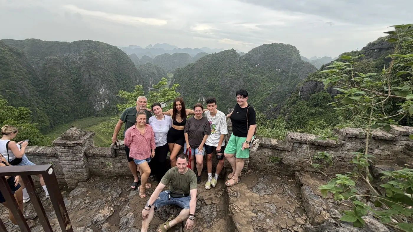 Group of travelers posing on a stone viewpoint above green limestone mountains