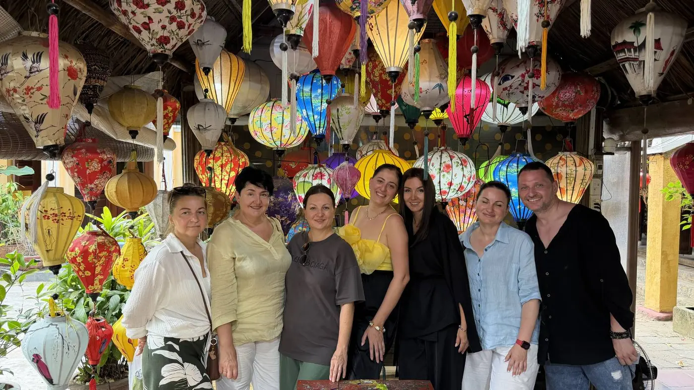 Seven people standing under colorful silk lanterns in a Hoi An lantern workshop