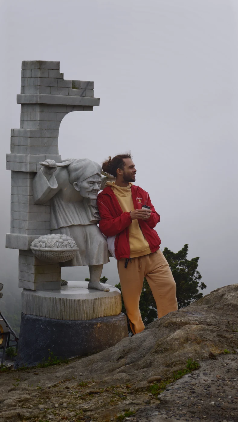 Traveler standing beside a stone farmer statue on a foggy summit