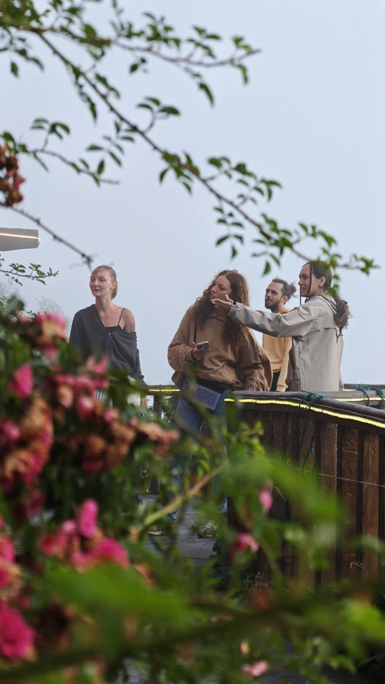 Group of travelers admiring misty mountains from a flower-lined terrace