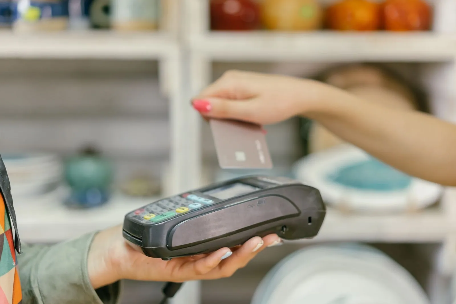 A hand tapping a bank card on a card terminal held by a shop assistant
