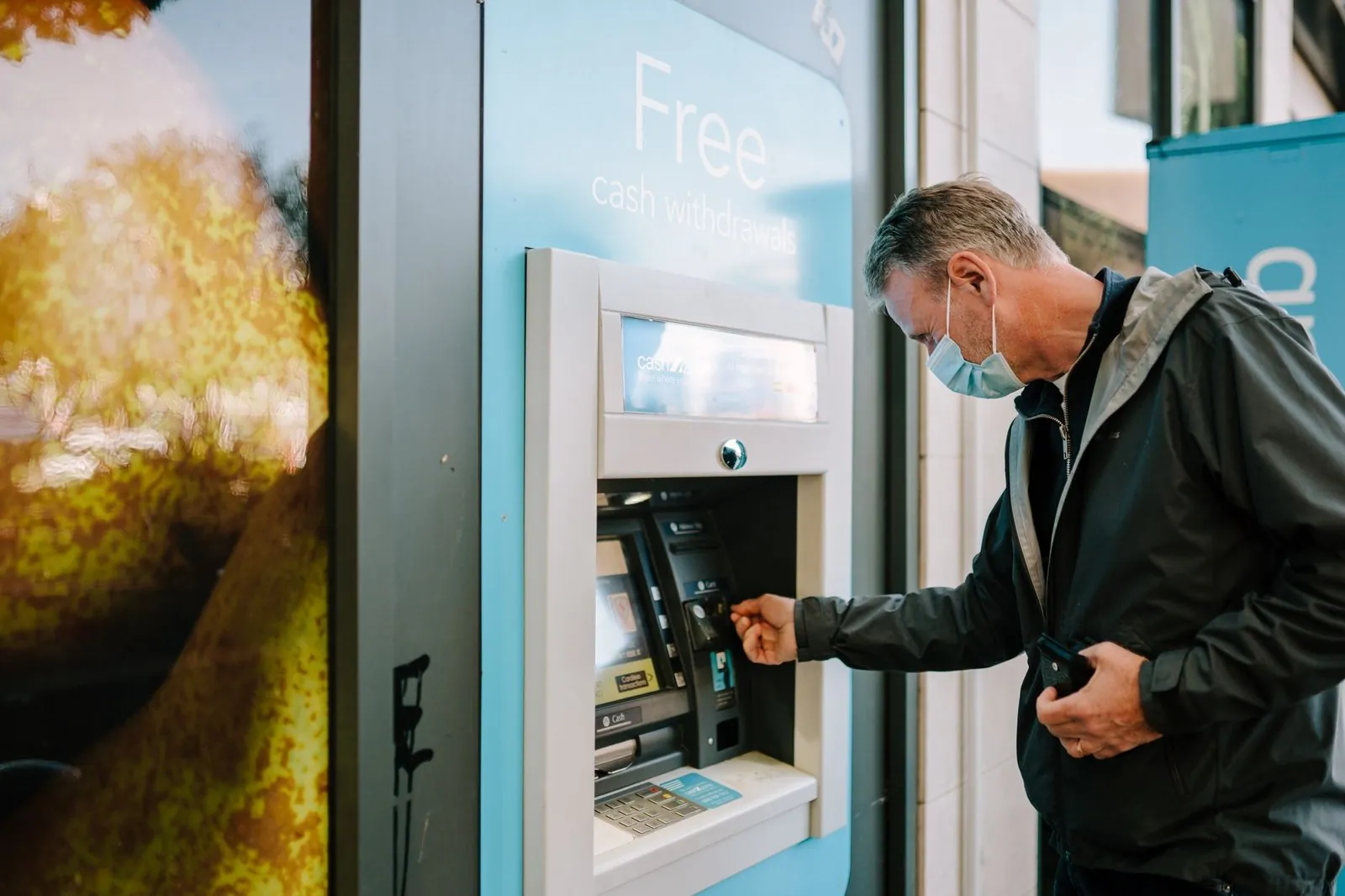 A man withdrawing cash at a street ATM marked free cash withdrawals