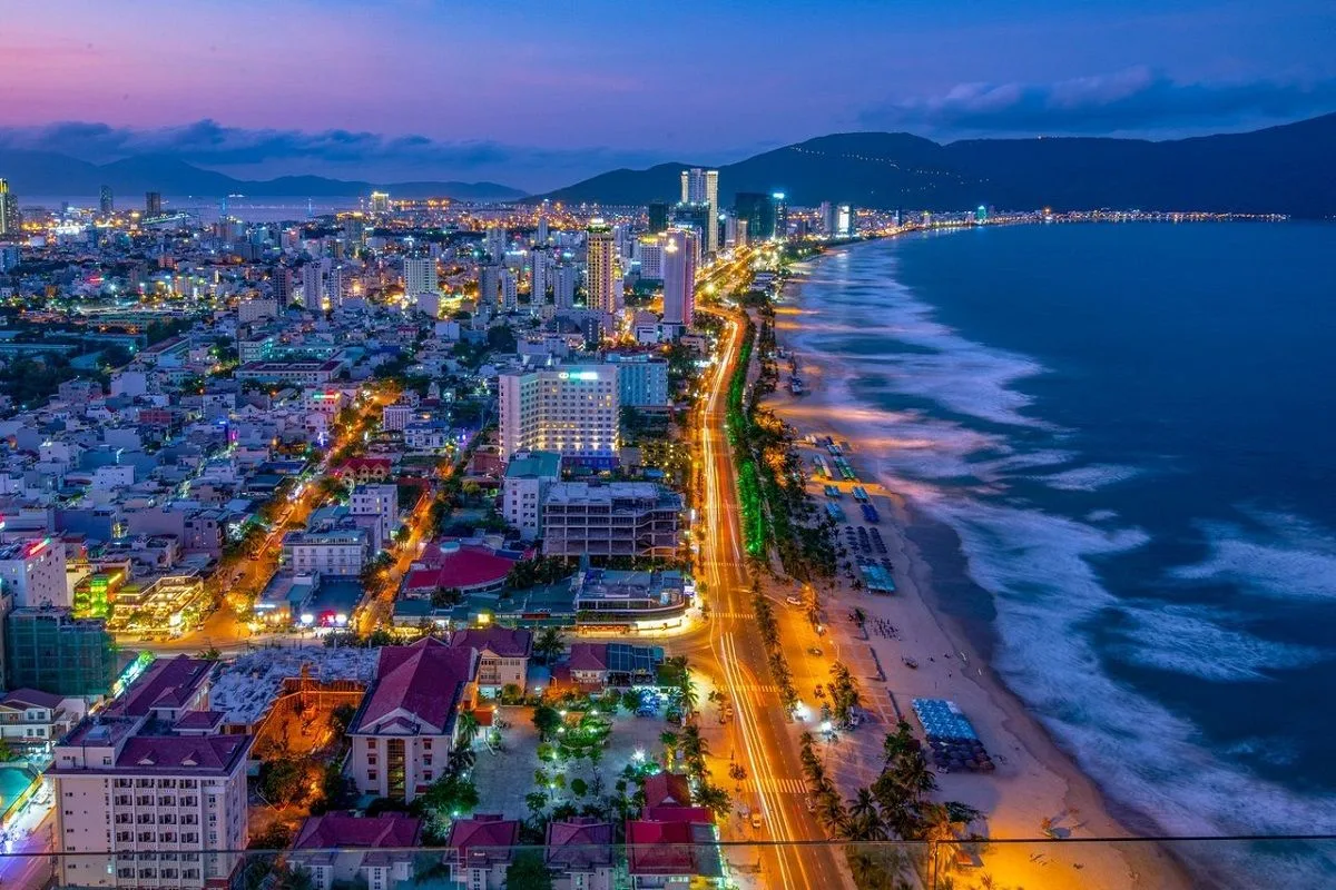 Aerial view of a Vietnamese beach and city lights at night with mountains behind