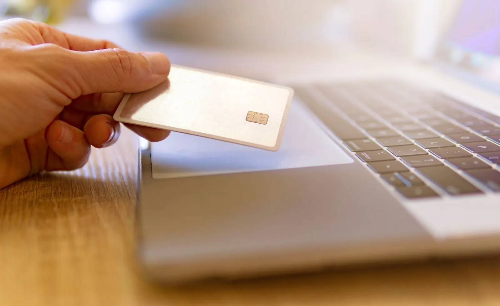 Hand holding a bank card beside an open laptop to pay an online visa fee
