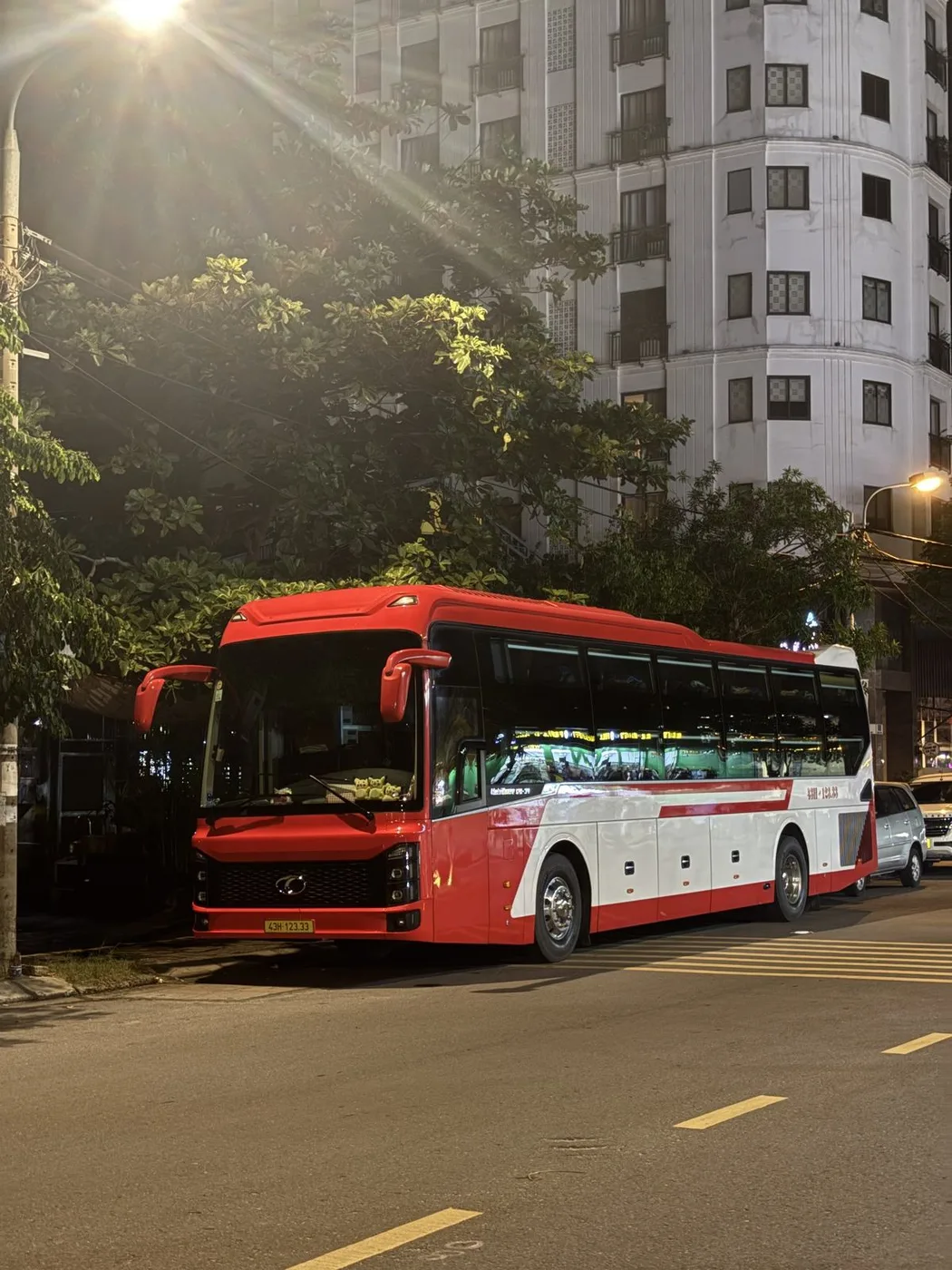 Red and white sleeper bus parked on a Da Nang street