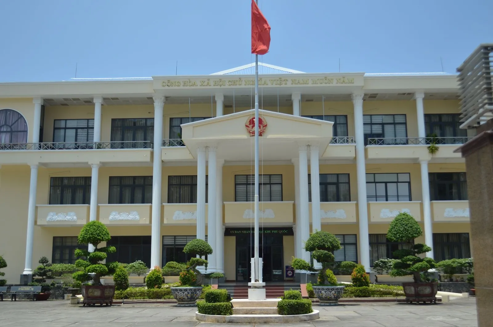 Yellow colonial-style Vietnamese government building with a red national flag