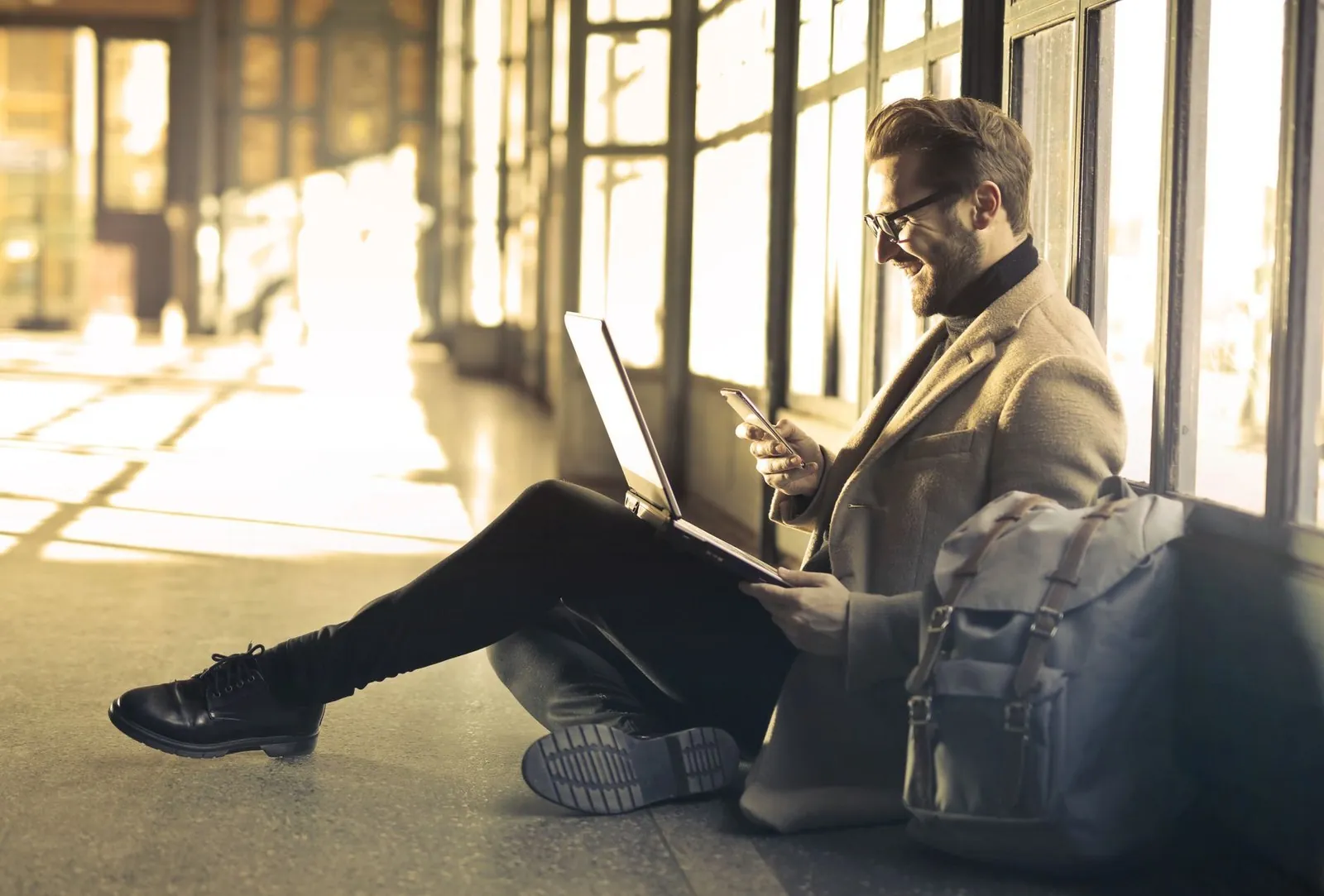 Traveler using a laptop and phone while sitting with a backpack