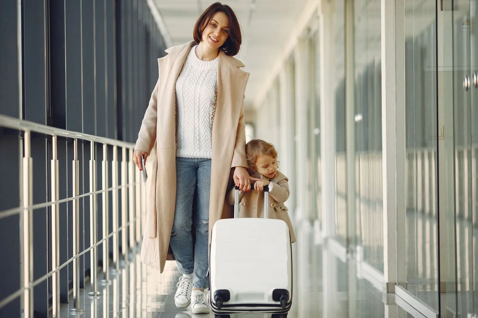 Mother and daughter walking through an airport with a suitcase