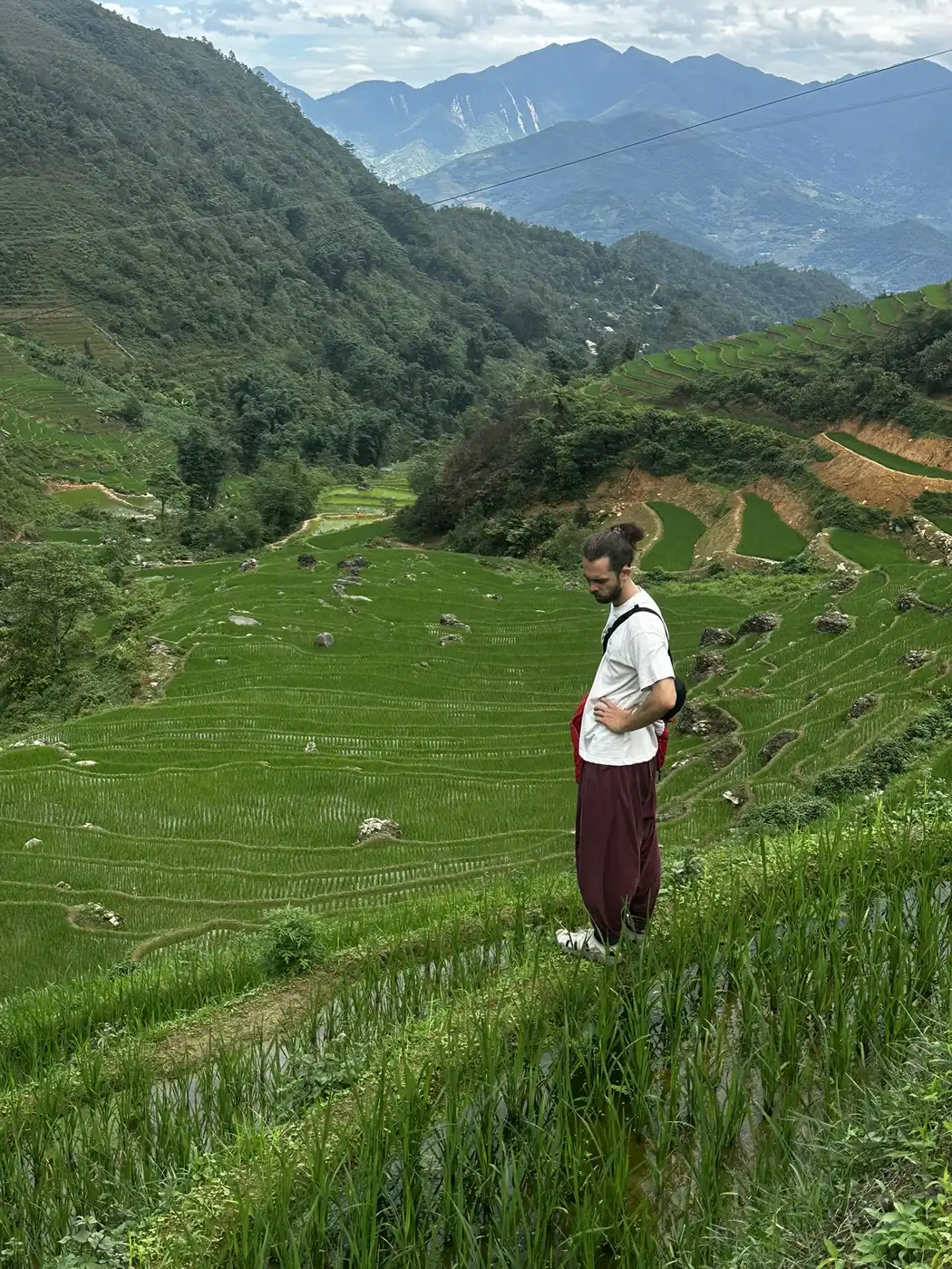 Traveler walking a narrow trail beside green rice terraces in Sa Pa
