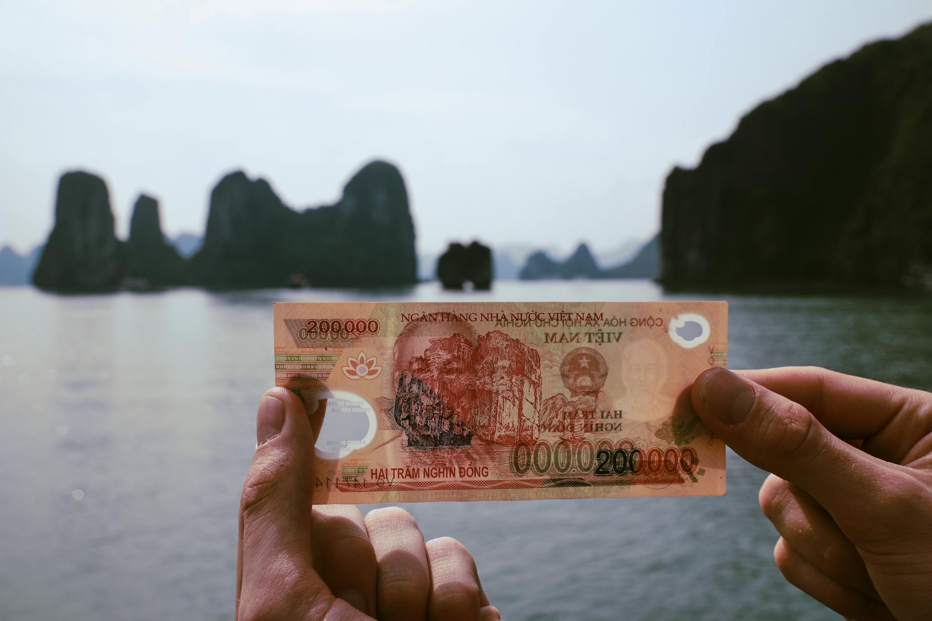 A 200,000 VND banknote held against Halong Bay — cash in dong is the working currency at the counter