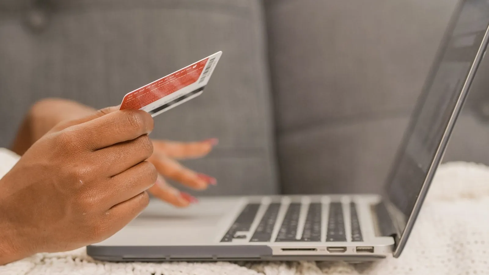 Hand holding a credit card in front of an open laptop