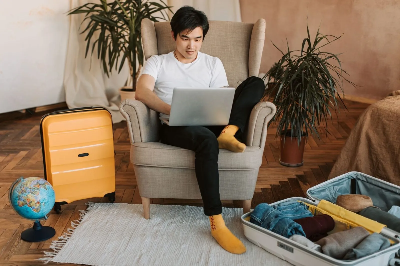 Man planning travel on a laptop with a suitcase and globe nearby