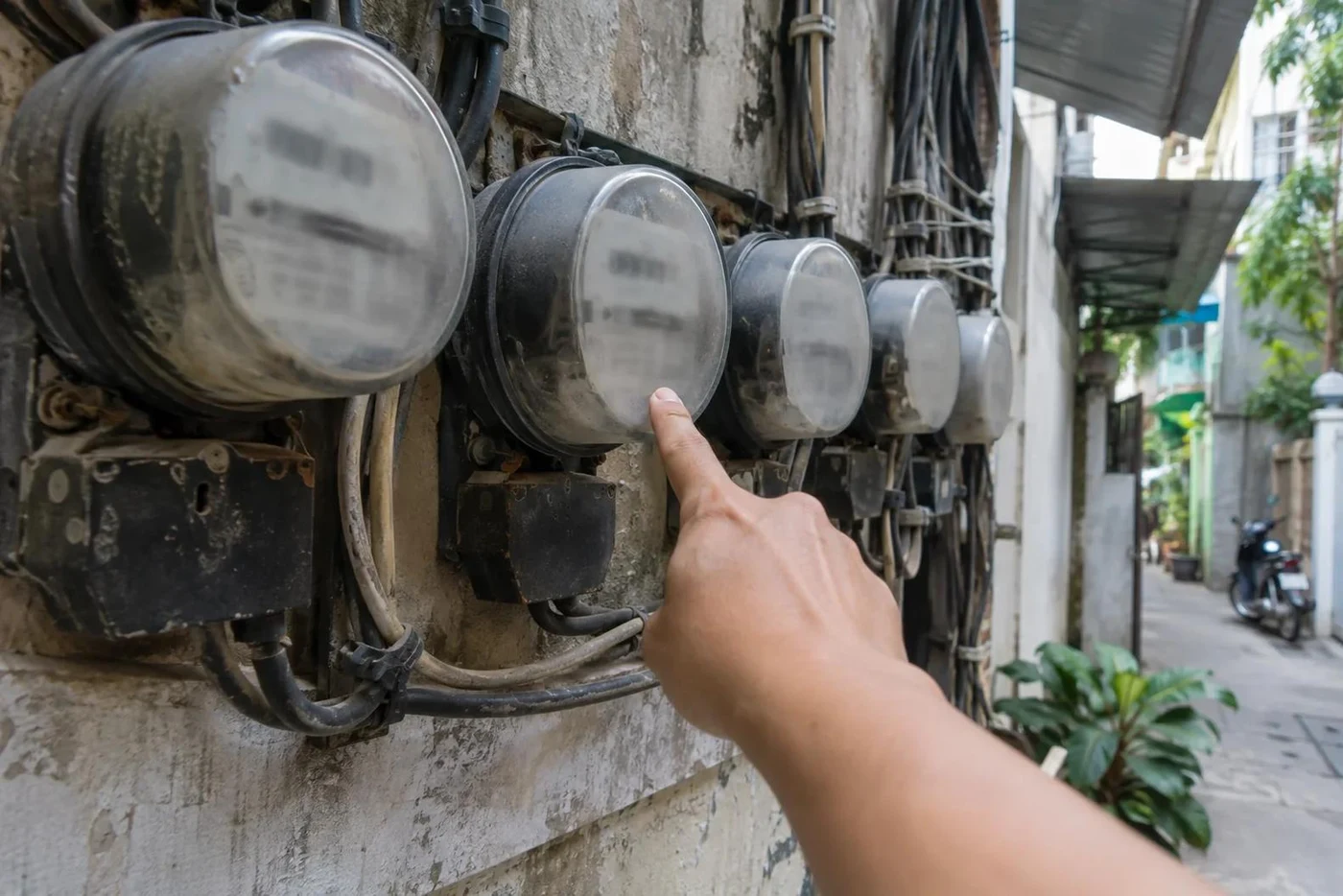 Row of old electricity meters on a wall with a hand pointing at one
