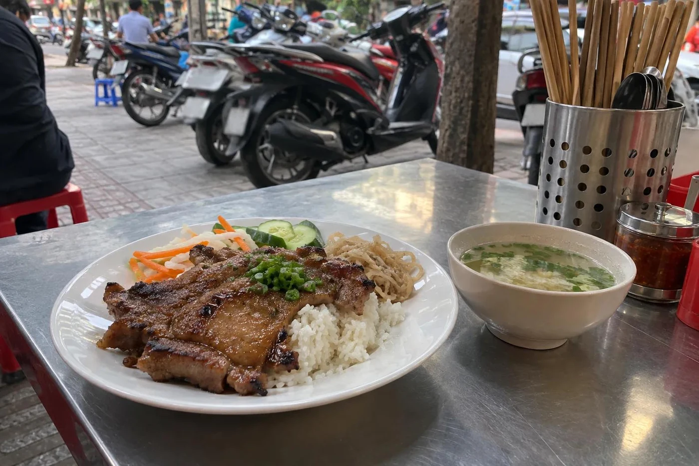 Plate of grilled pork with rice and a bowl of soup at a street table