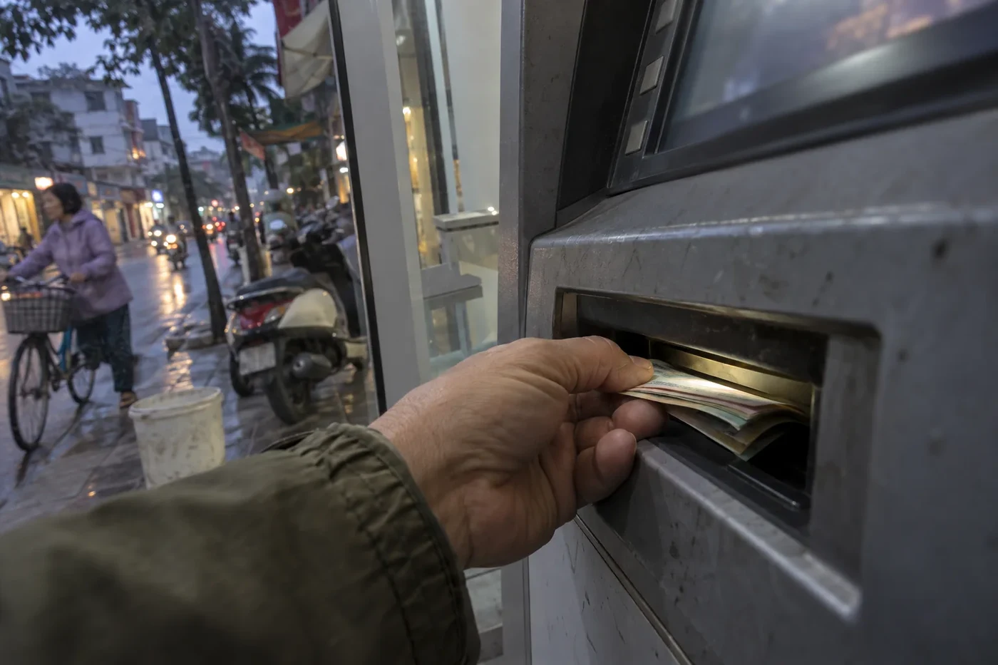 Hand pulling banknotes out of a street ATM slot in the evening rain