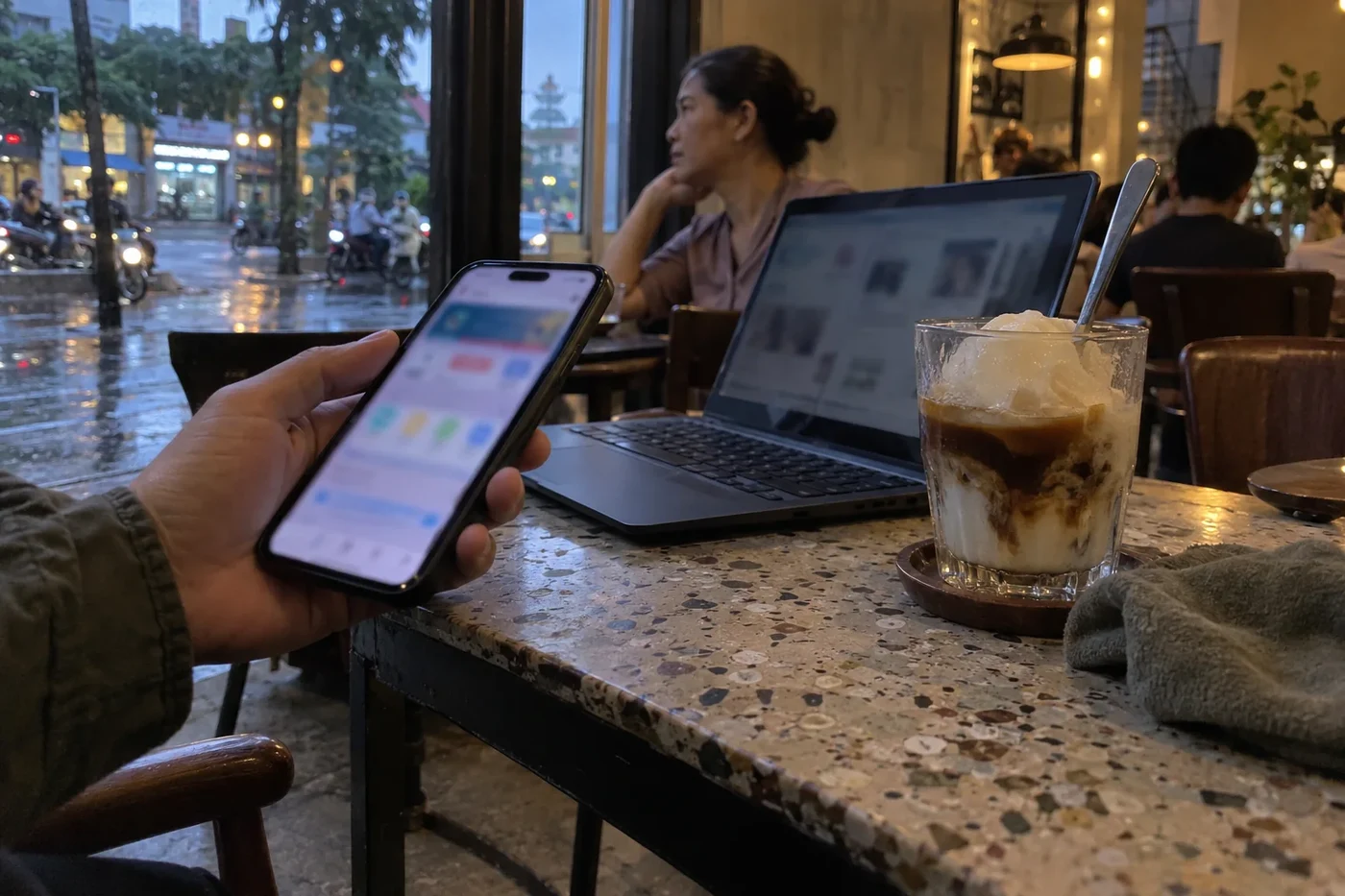 Hand holding a smartphone with a payment app open at a cafe table beside a laptop
