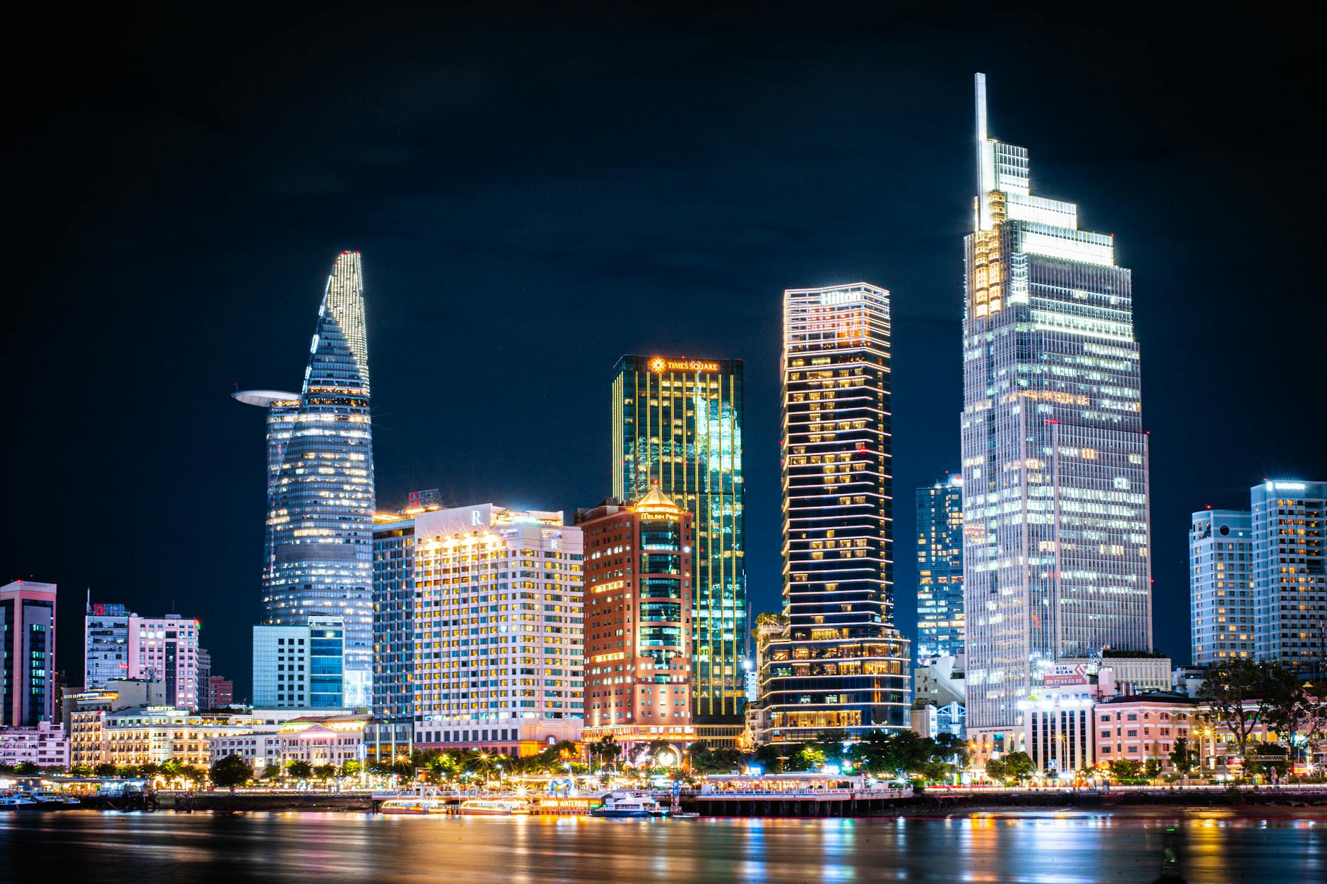 Ho Chi Minh City night skyline with Bitexco Financial Tower and illuminated skyscrapers reflected in the Saigon River