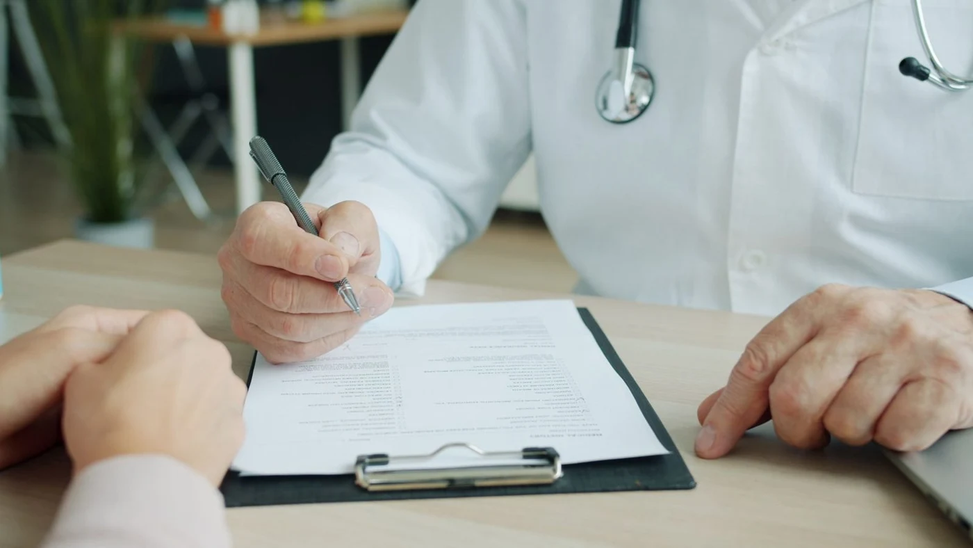 Doctor with a clipboard talking to a patient in a pink sweater