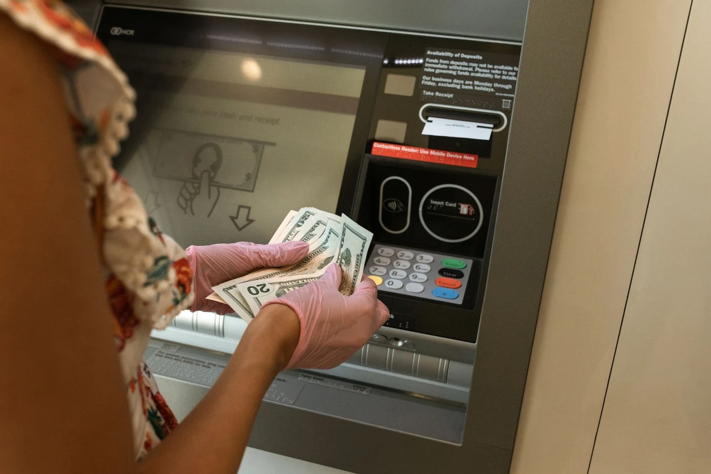 Woman holding US dollar bills in front of a bank ATM