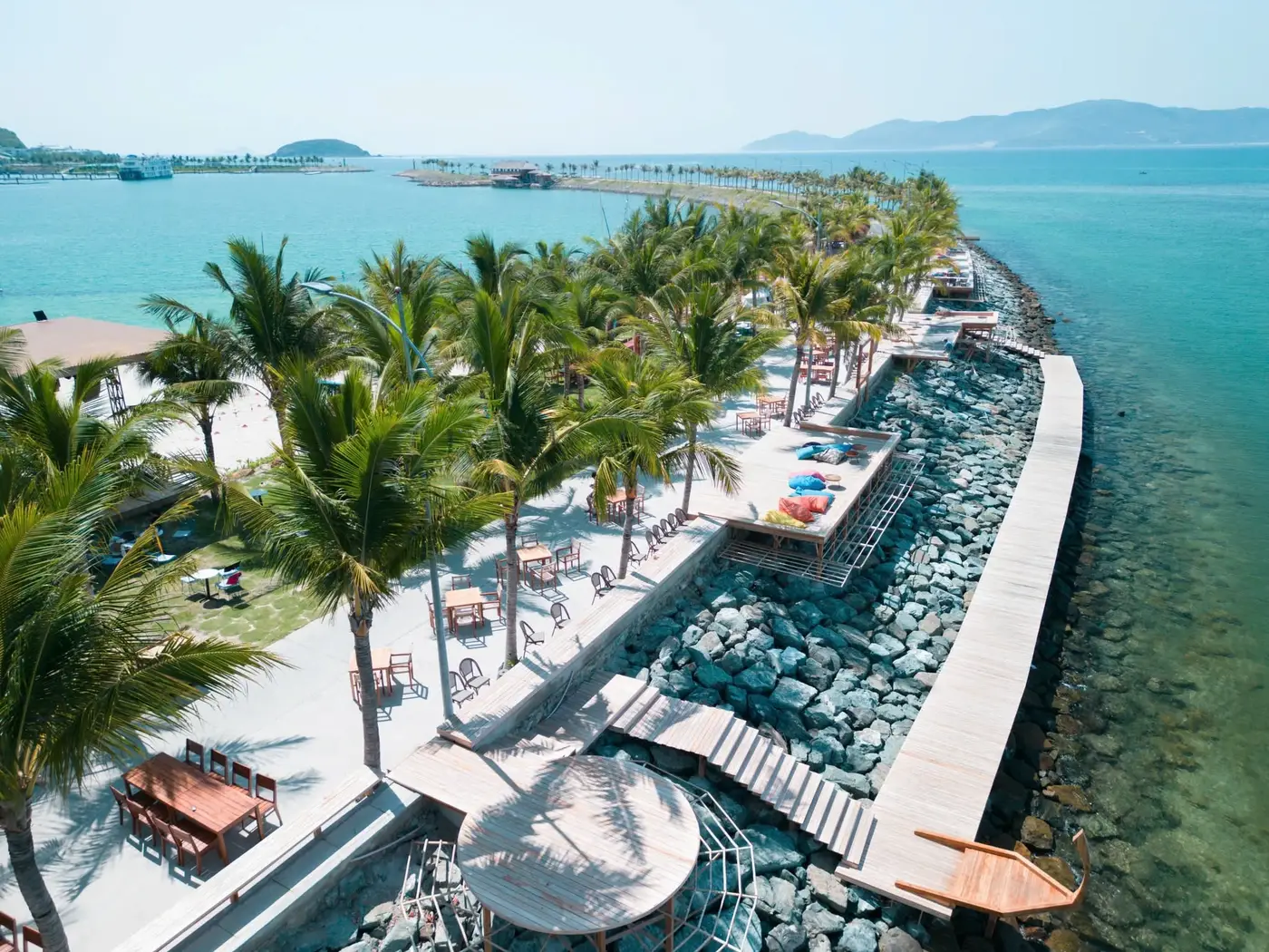 Aerial view of a seafront promenade with palms and a wooden boardwalk