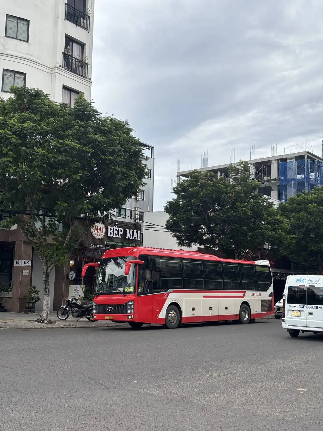 Red and white sleeper bus pulling onto a city street in Da Nang